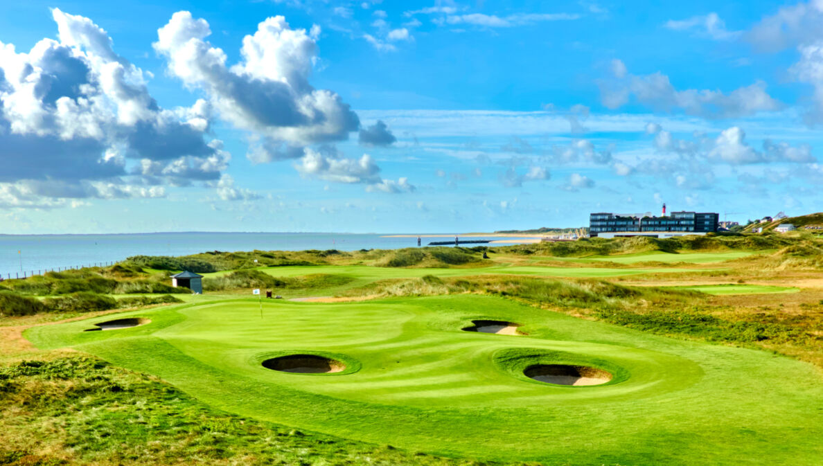 Grüner Golfplatz mit runden Bunkern mit Hotel und Meer im Hintergrund