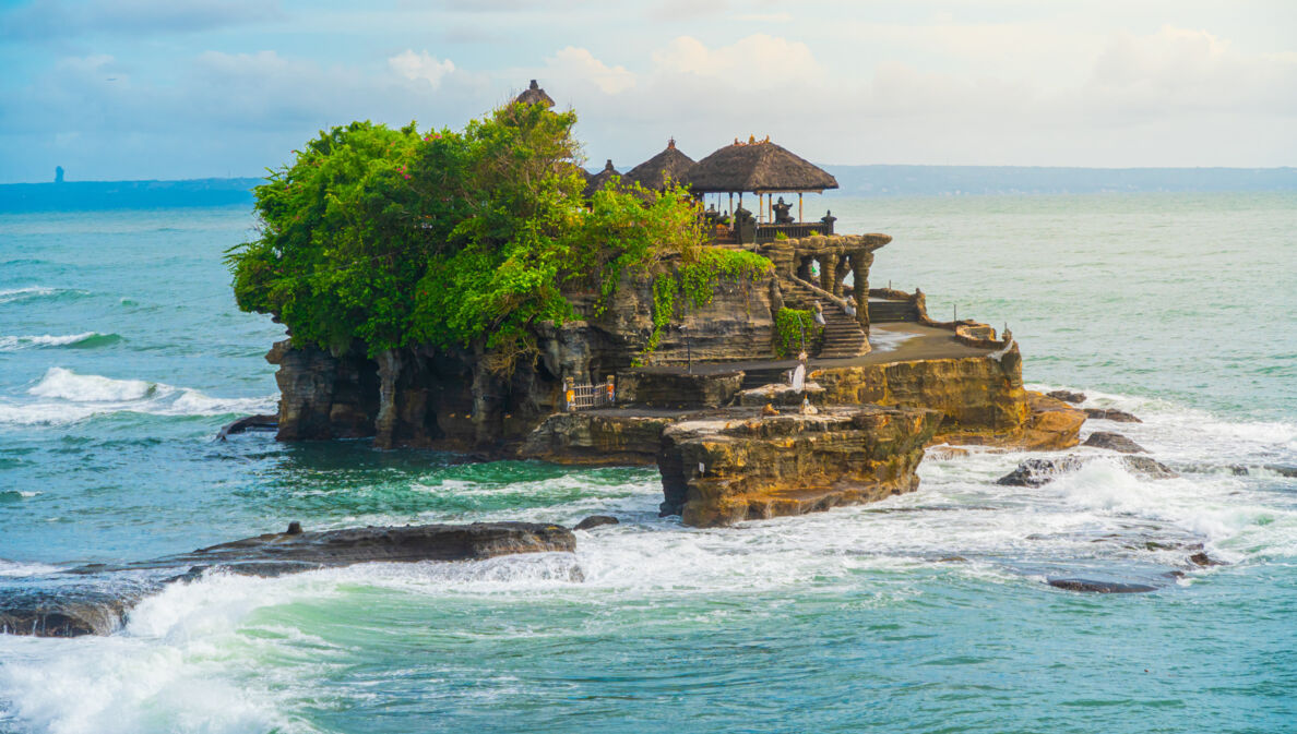 Ein Tempel und mehrere Bäume auf einem Felsen im Meer