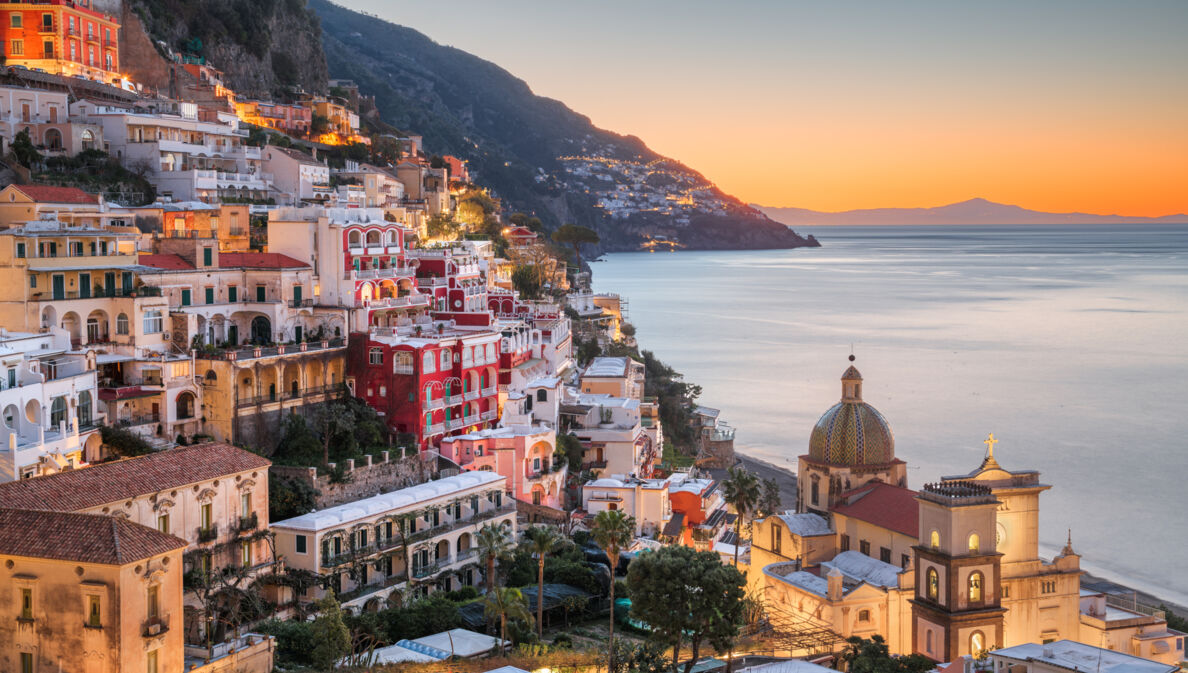 Das Dorf Positano am Hang eines gebirgigen Küstenabschnittes bei Sonnenuntergang