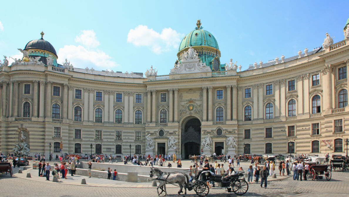 Personen und Pferdekutschen auf einem Platz vor der Wiener Hofburg