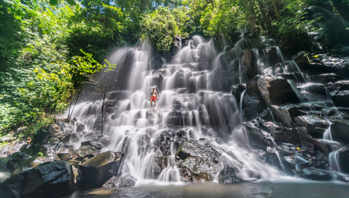 Eine Person in roter Badehose steht in einem gestuften Wasserfall