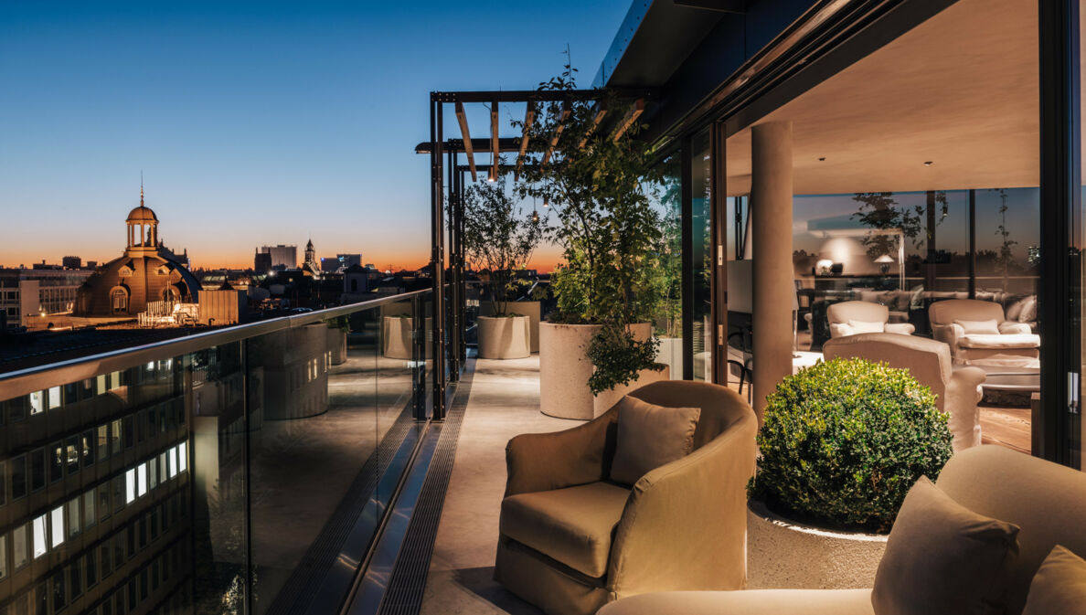 Dachterrasse mit hellen Polstermöbeln vor der Skyline Münchens bei Sonnenuntergang.