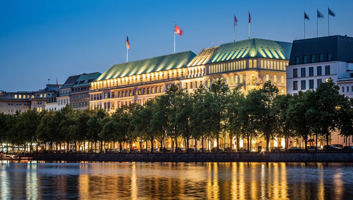 Beleuchtete Außenfassade des Hotels Vier Jahreszeiten am Wasser in der Dunkelheit.