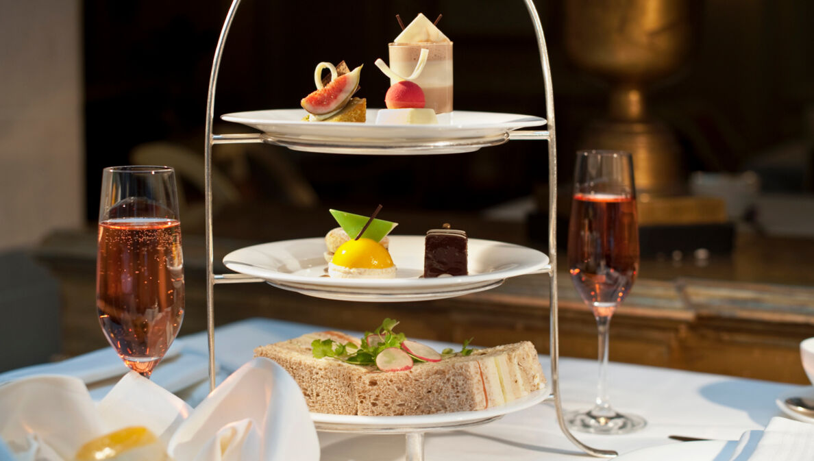 Eine Etagere mit süßen und herzhaften Häppchen auf einem edel gedeckten Tisch neben zwei Champagnergläsern