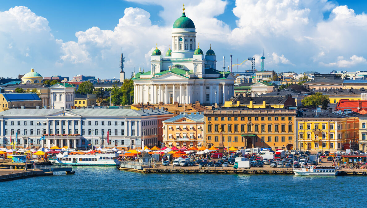 Blick auf eine Stadt am Wasser mit bunten Häusern und einer weißen Kathedrale im Mittelpunkt.