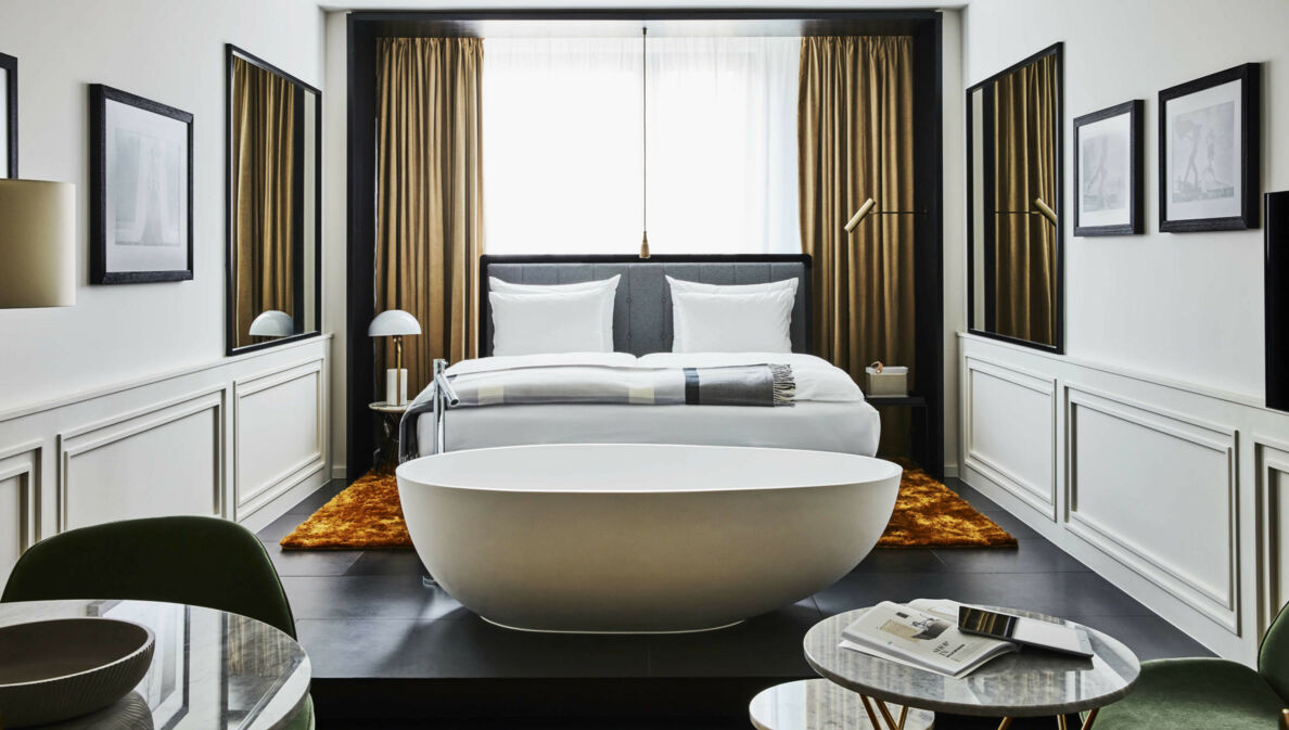 Moderne Hotelsuite mit einer freistehenden Badewanne vor einem Doppelbett.