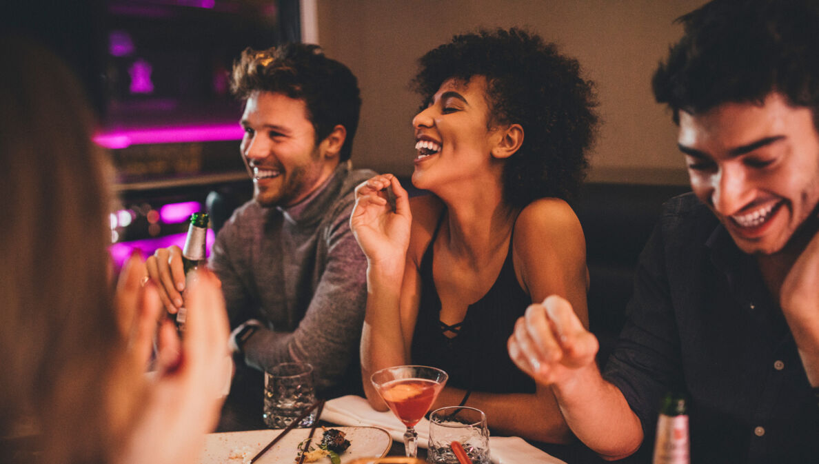 Eine Gruppe junger Menschen sitzt gut gelaunt mit Getränken an einem Tisch in einem Restaurant.