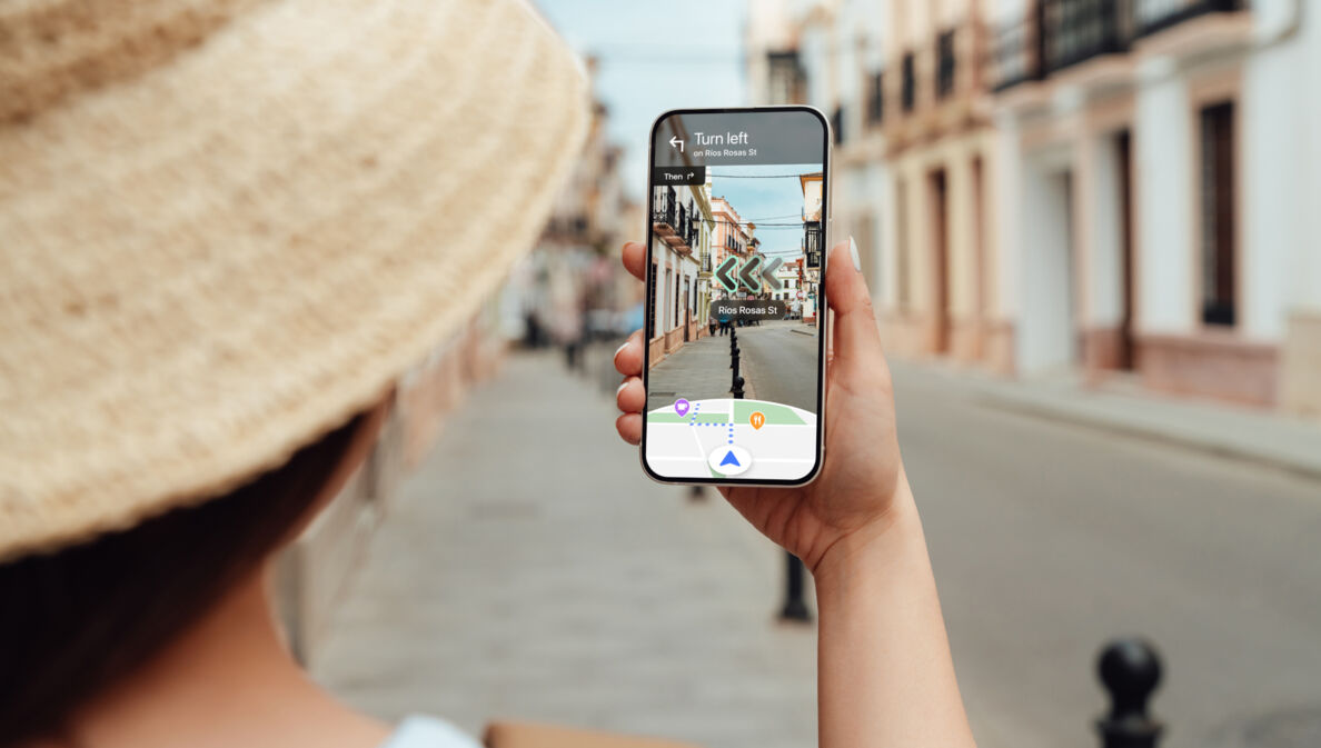 Eine Frau navigiert mit Blick auf ihr Smartphone per Live View von Google Maps durch eine Straße.