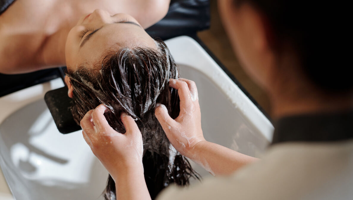 Die Haare einer liegenden Frau werden an einem Waschbecken von einer anderen Person gewaschen.