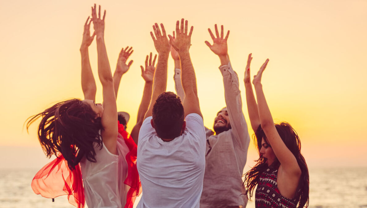 people dancing at the beach with hands up. concept about party, music and people