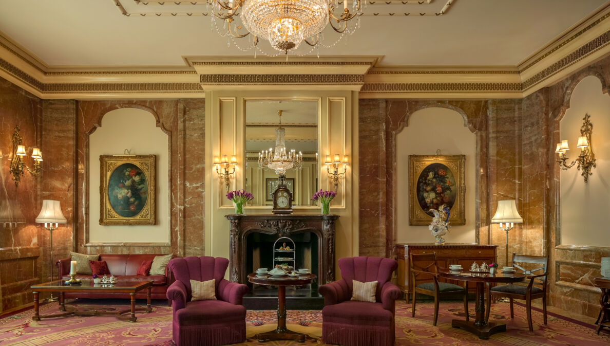 Edle, altehrwürdige Hotel Lobby Lounge mit Teppichboden, Goldverzierungen und roten Polstermöbeln unter einem Kronleuchter.