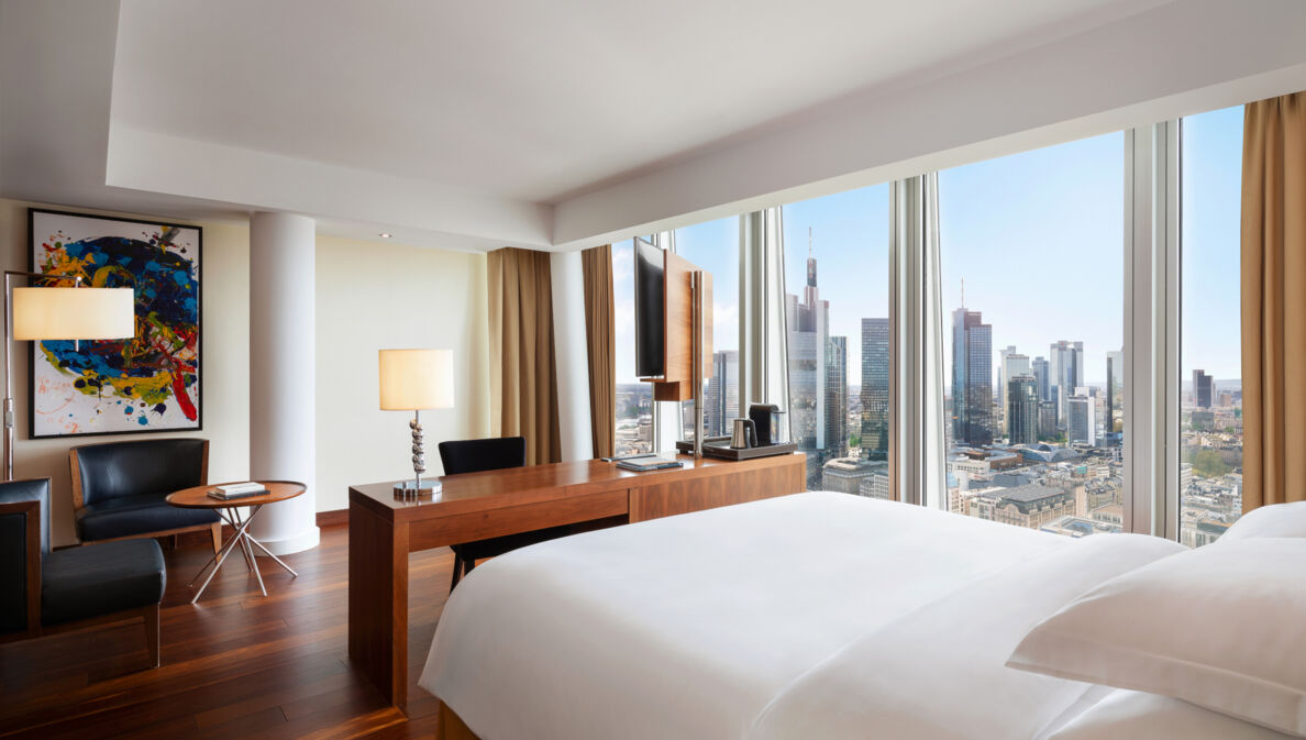 Modernes Hotelzimmer mit Blick auf die Frankfurter Skyline durch bodentiefe Panoramafenster.