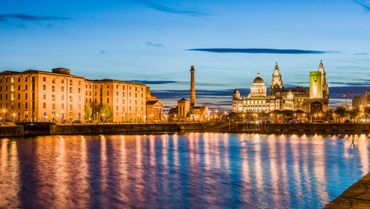 Waterfront in Liverpool bei Nacht mit beleuchteten Gebäuden im Hintergrund.