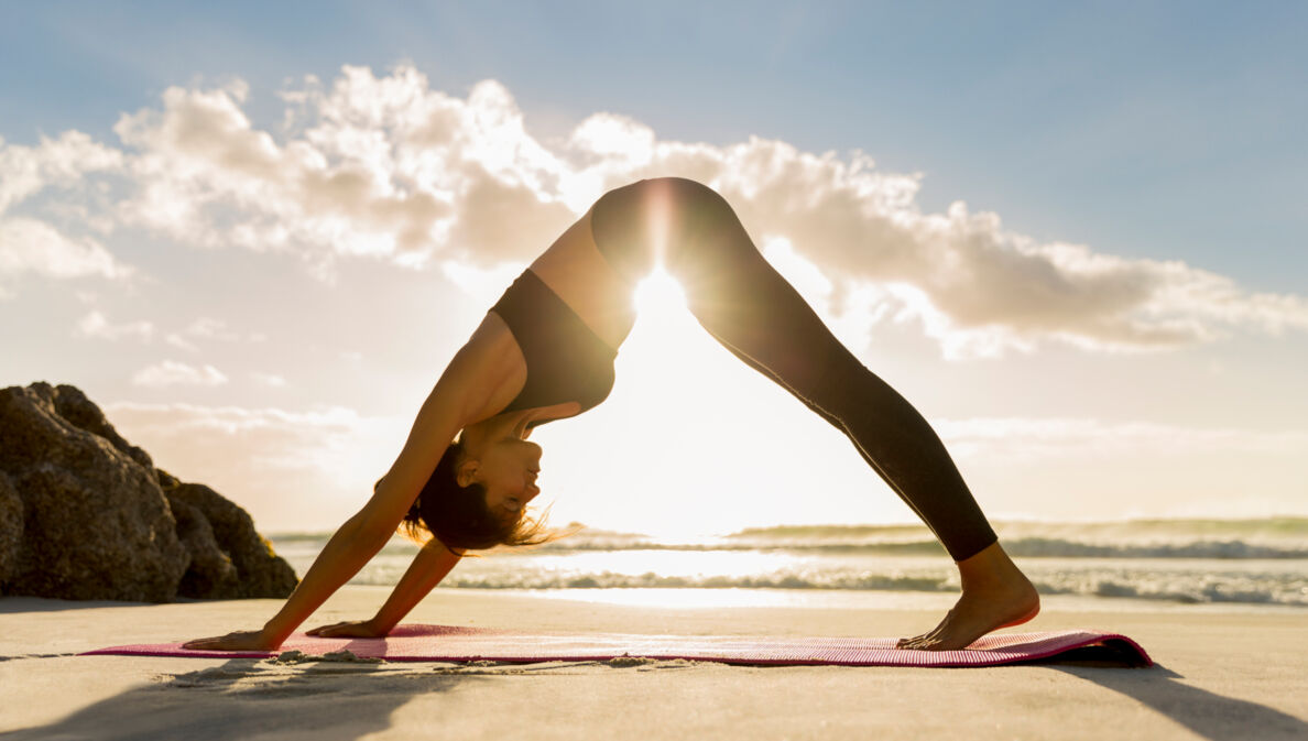 Eine Frau in einer Yoga-Pose am Strand. 