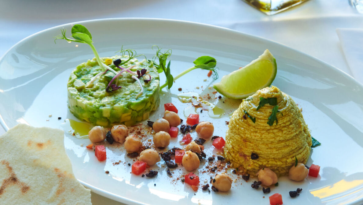 Ein weißer Porzellanteller mit einem Gericht aus Avocado, Kichererbsen, Limette und mehr im Restaurant brenner.