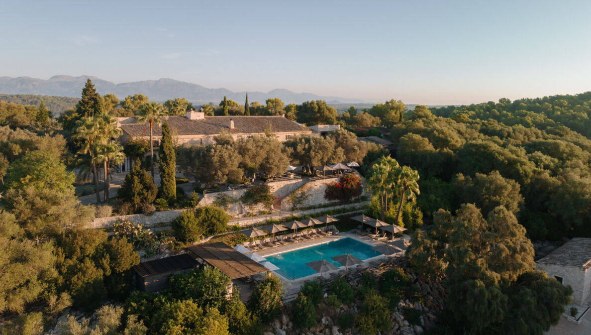 Luftaufnahme einer Finca mit Pool inmitten einer bewaldeten Hügellandschaft.