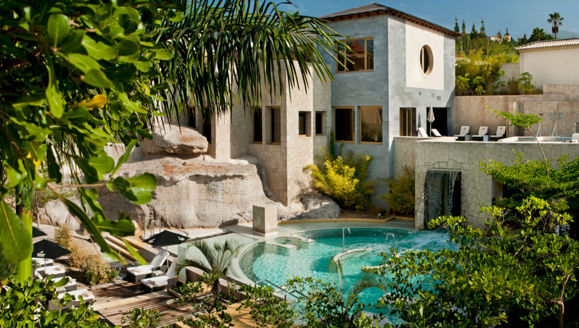 Resort des Bahia del Duque auf Teneriffa mit Poolanlage, Begrünung, Holzterrasse und Liegen.