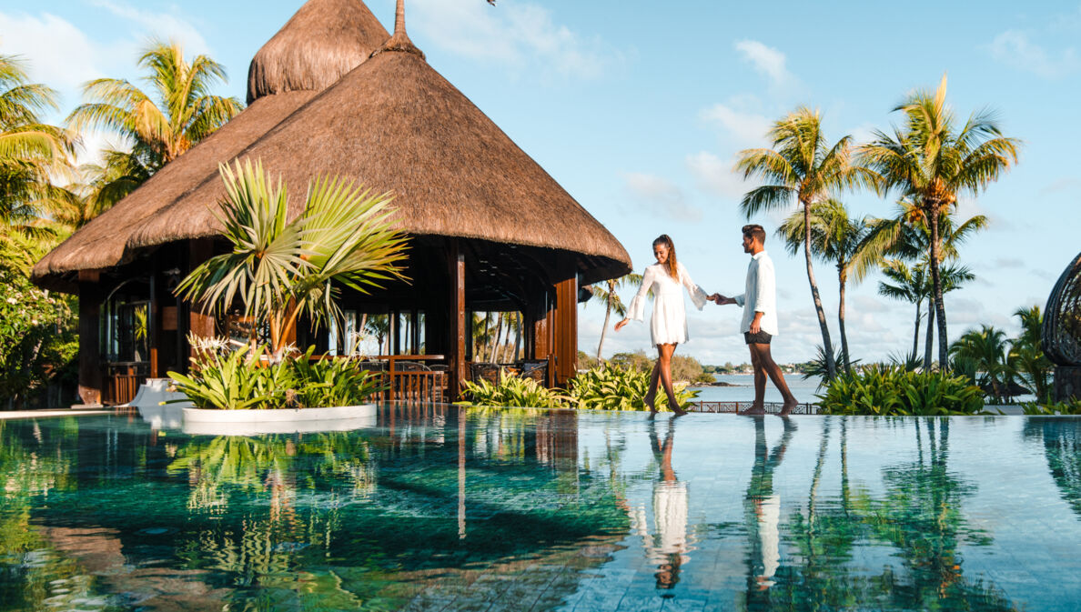 Ein Paar steht an einem luxuriösen Hotelpool am Meer in tropischer Umgebung.