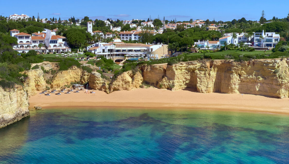 Luftaufnahme der Hotelanlage des Vila Vita Parc, das direkt an einer Klippe liegt. Darunter befindet sich ein Sandstrand und türkisblaues Meer.