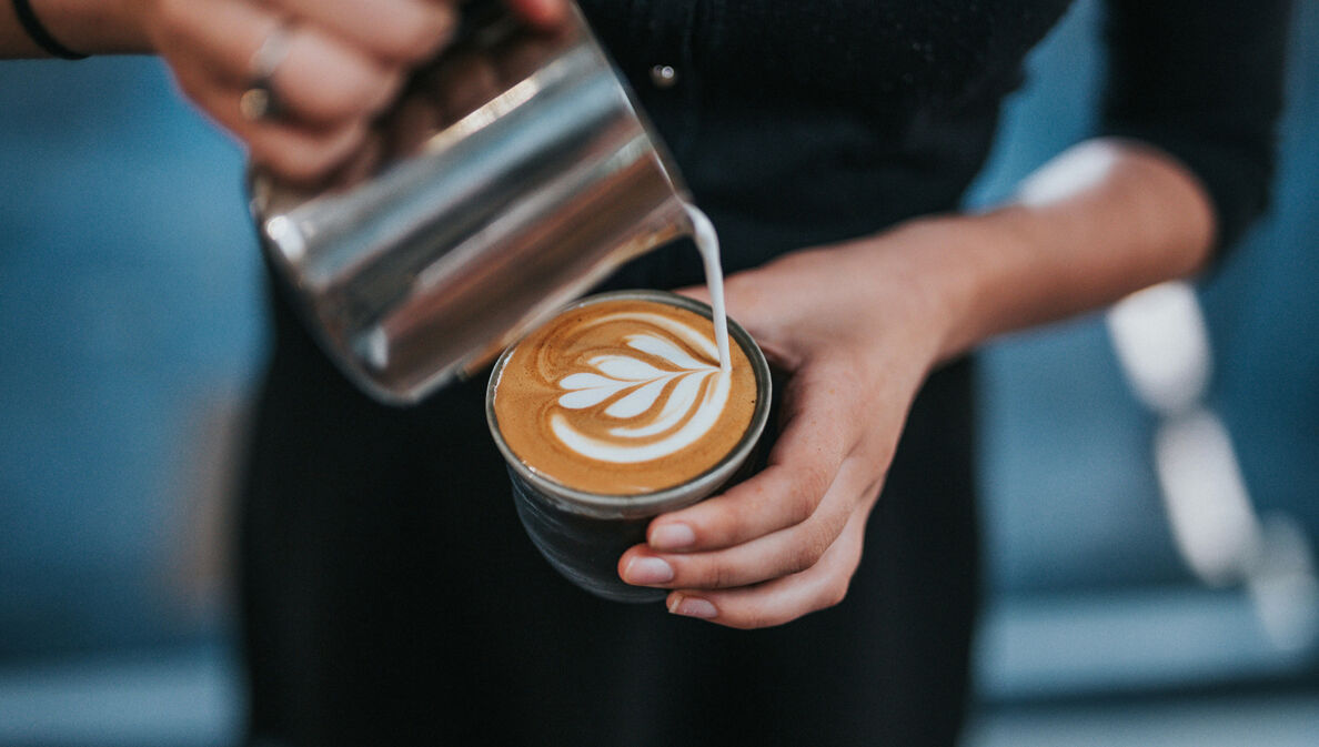 Milchschaum wird in einen Becher Kaffee geschüttet