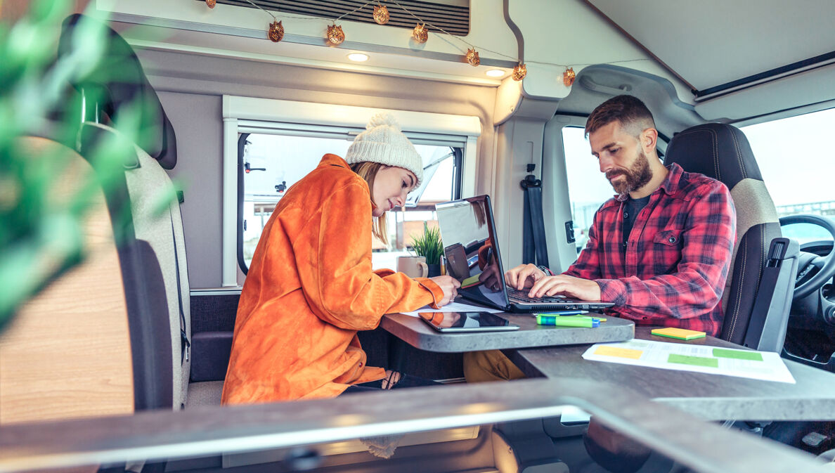 Junges Paar arbeitet am Laptop im Wohnmobil