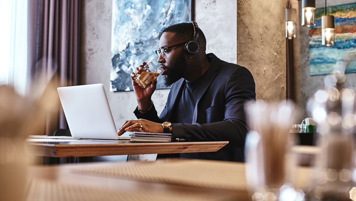 Geschäftsmann mit Kopfhörer arbeitet in einer Hotellobby am Laptop