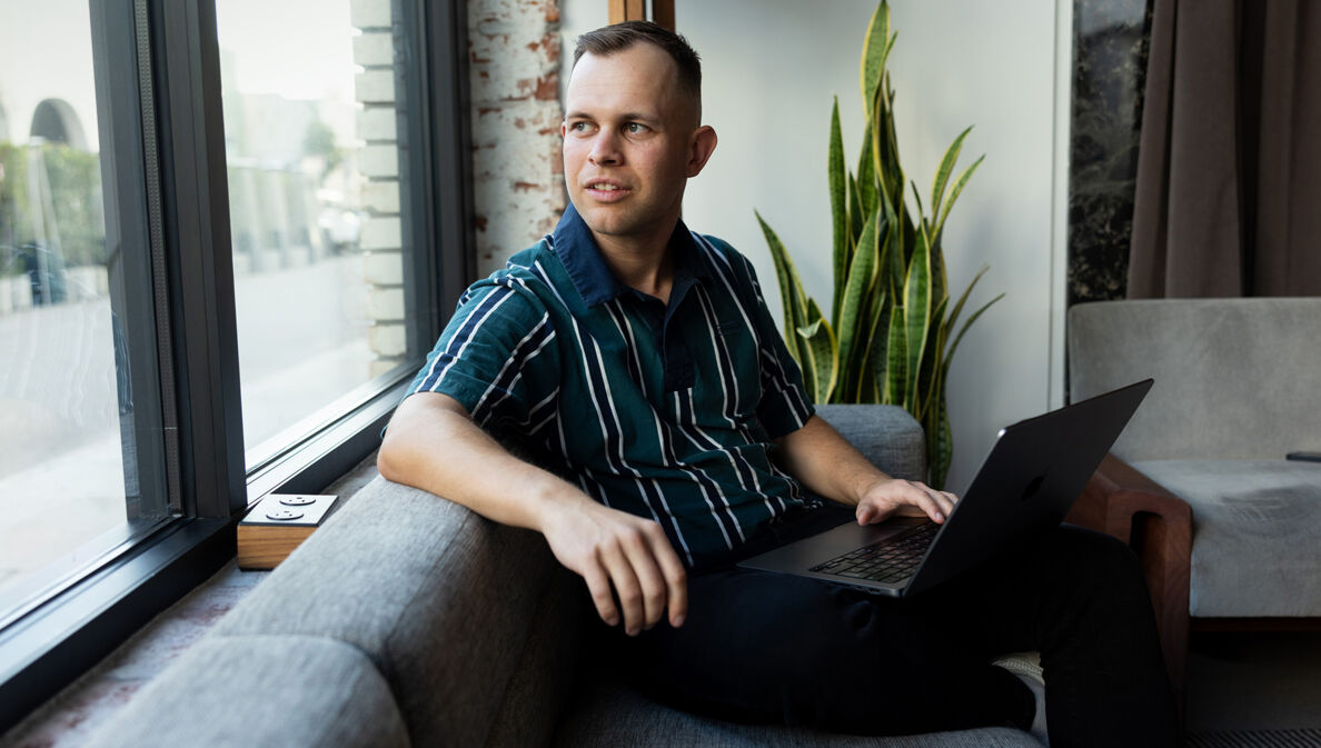 Benjamin Diedering sitzt mit Laptop auf dem Sofa und schaut aus dem Fenster