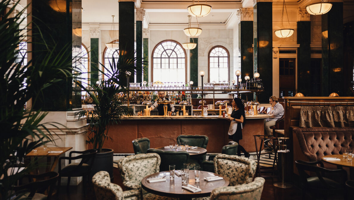 Hotellobby mit grünen Säulen um eine Bar mit Esstischen im 1920er-Jahre-Stil.