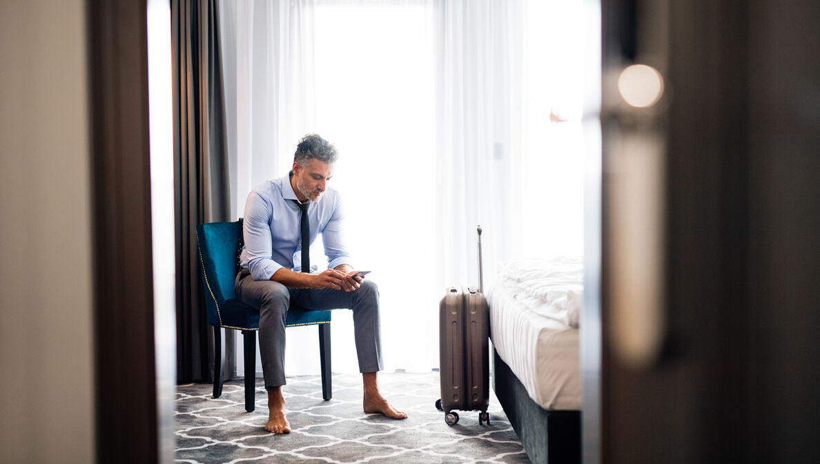 GEschäftsmann im Hotelzimmer schaut auf sein Smartphone