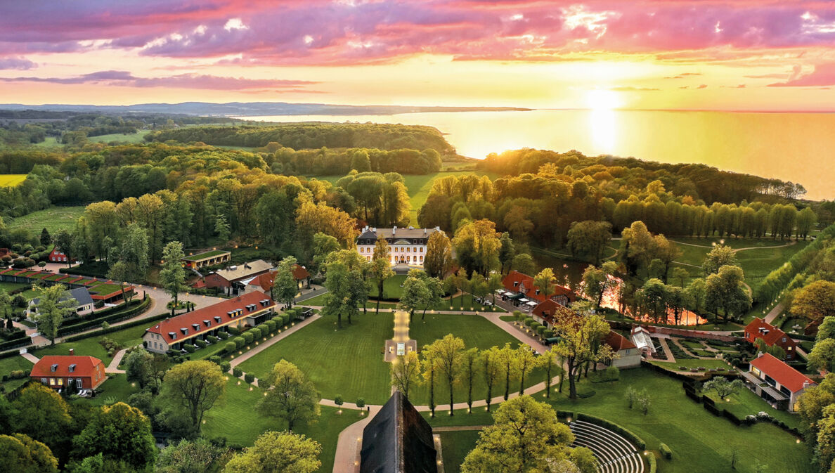 Luxuriöses Hotelresort mit Park- und Waldlandschaft an Meeresküste bei Sonnenuntergang.