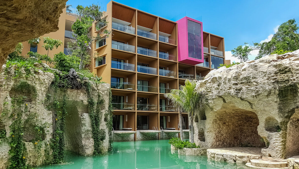 Moderner Hotelkomplex, umgeben von bepflanzten Felsen an einem Pool mit türkisfarbenem Wasser.