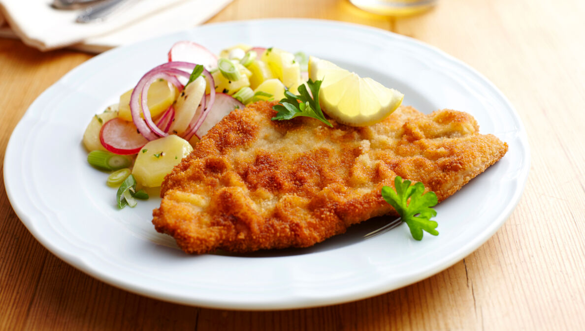 Ein paniertes Schnitzel mit Kartoffelsalat auf einem weißen Teller.