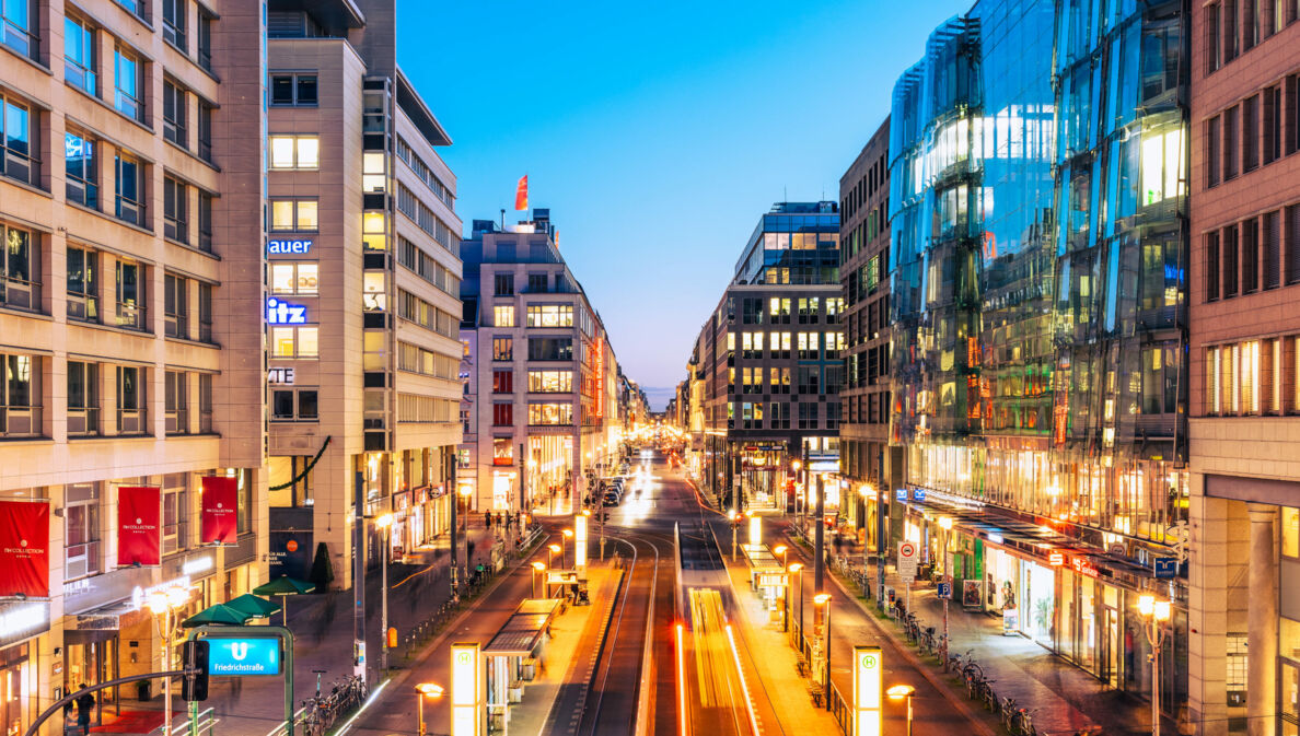 Einkaufsstraße im Stadtzentrum mit beleuchteten Gebäuden bei Abenddämmerung.