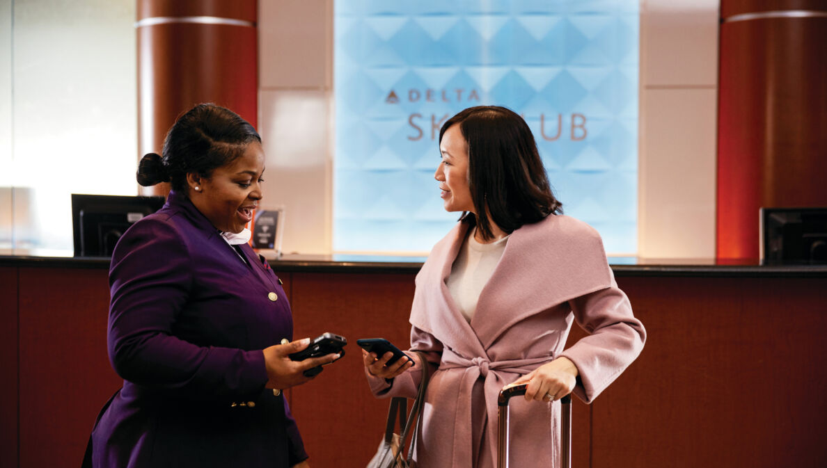 Zwei Frauen mit Smartphones am Empfang einer Delta Sky Club Lounge.