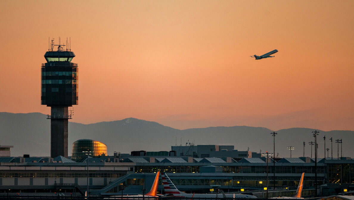 Tower des Vancouver Airports bei Sonnenuntergang und ein startendes Flugzeug.