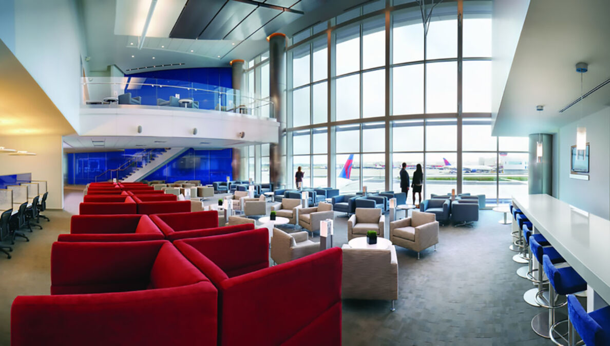 Geräumige Flughafen-Lounge in den Farben Rot, Weiß und Blau mit Blick aufs Rollfeld durch Panoramafenster.