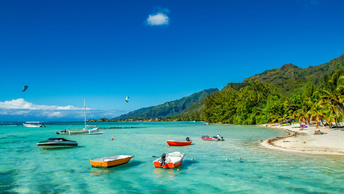 Kleine Boote im türkisblauen Wasser an einem Sandstrand mit tropischer Vegetation.