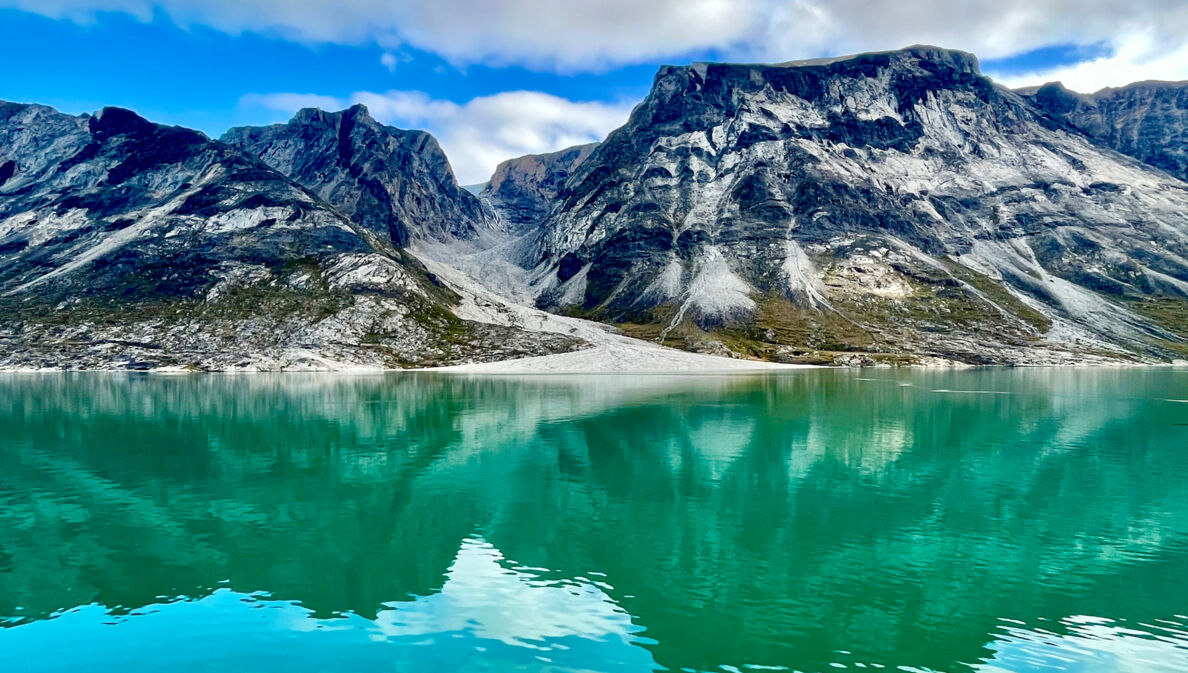 Das Bild zeigt dunkle Berge, die aus dem grün schimmernden Wasser des Prins Christian Sunds ragen. 