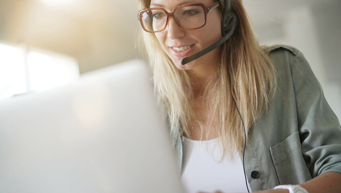 Eine blonde Frau mit Headset sitzt vor einem Laptop und arbeitet.