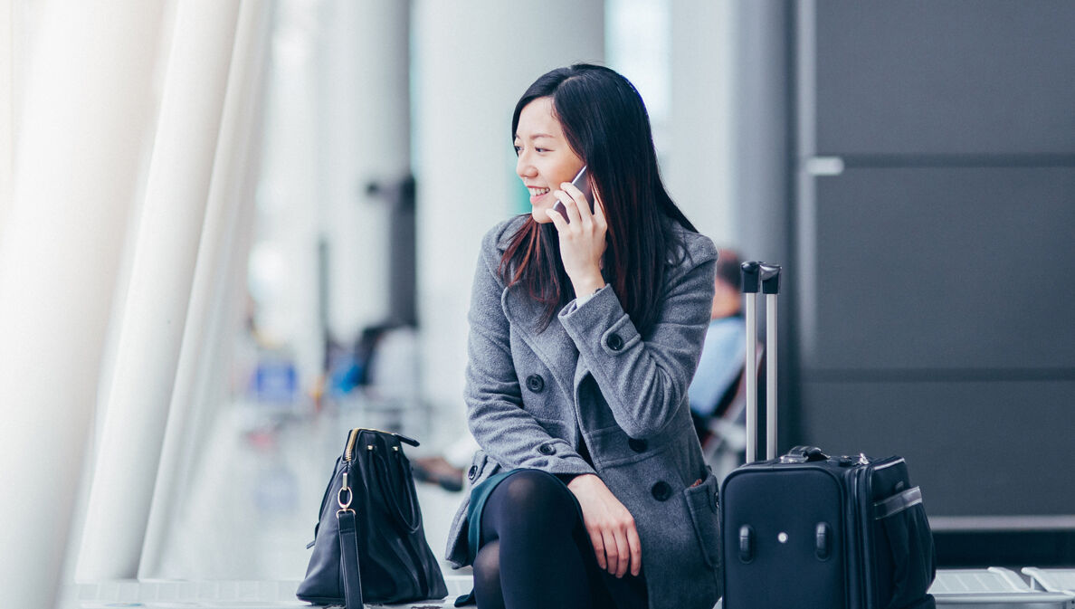 Eine asiatische Geschäftsfrau sitzt im Wartebereich eines Flughafens und telefoniert.