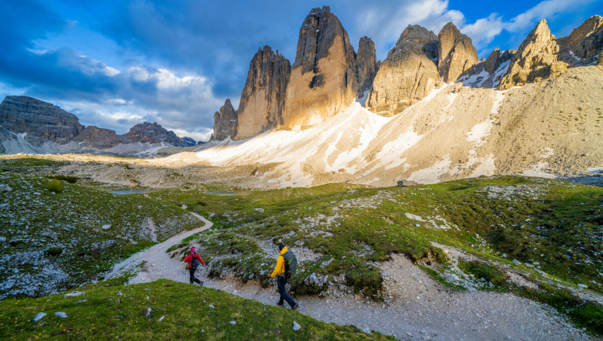 Zwei Personen beim Wandern, im Hintergrund Berge, blauer Himmel und Wolken.