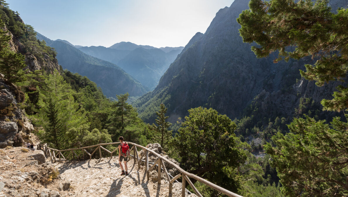 Eine Person beim Wandern in der Samaria-Schlucht auf Kreta, im Hintergrund Vegetation und Berggipfel.