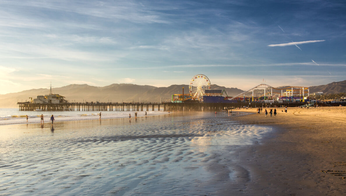 Ein Pier mit Freizeitpark an einem weitläufigen Sandstrand bei Sonnenuntergang.