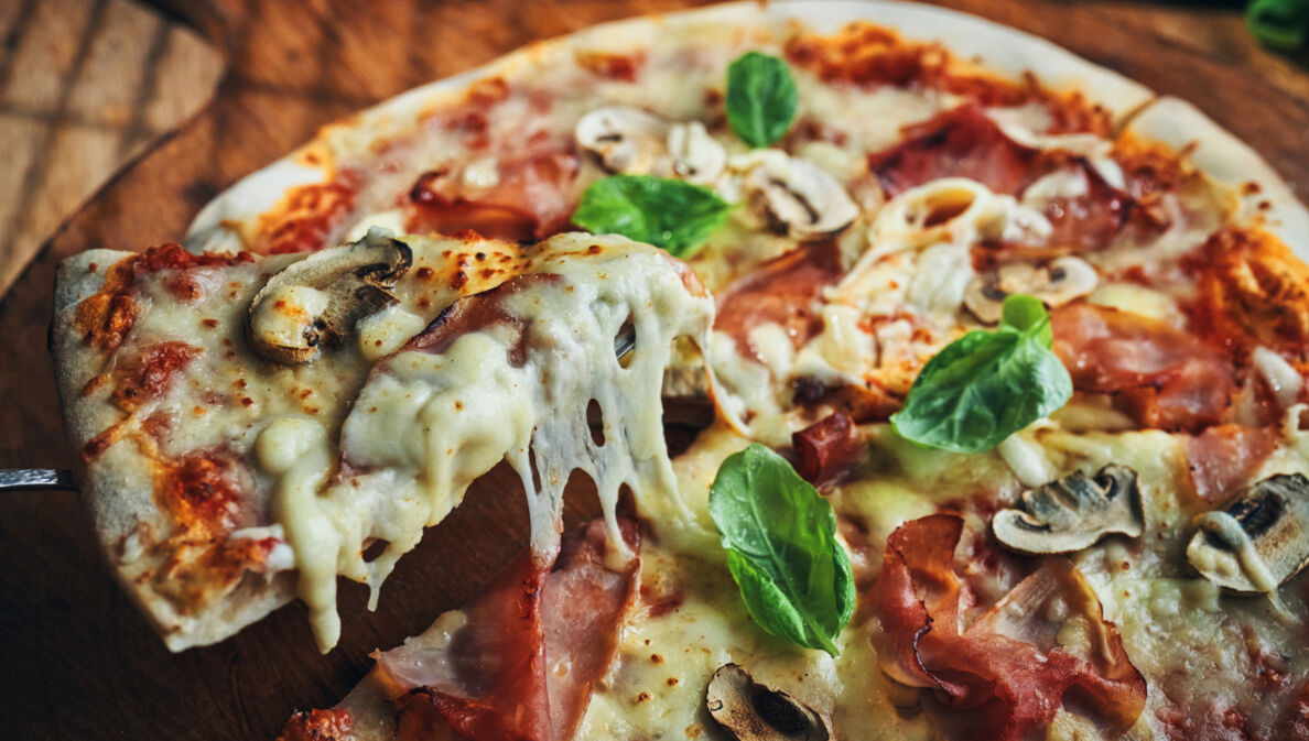 Nahaufnahme einer Pizza mit Champignons, Schinken und Basilikum auf zerlaufenem Käse.