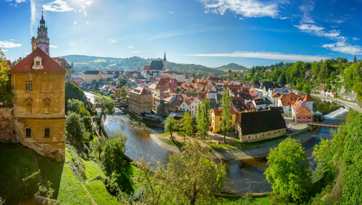 Mittelalterliche Kleinstadt mit Burg an einer Flussschlinge, umgeben von grünen Hügeln bei Sonnenschein.