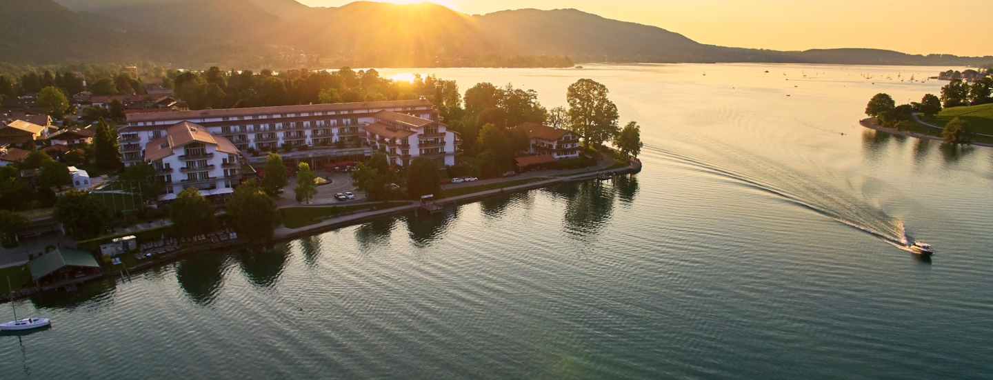 Luxuriöser Hotelkomplex an einem Seeufer, umgeben von Bäumen vor einer bewaldeten Hügellandschaft.