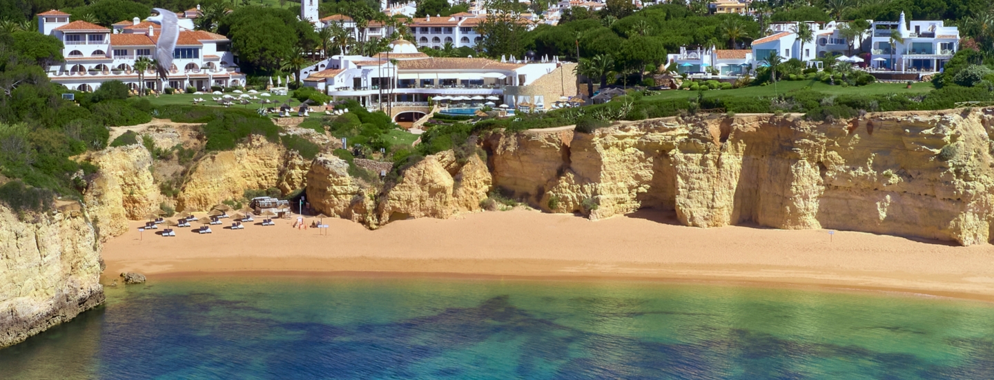 Luftaufnahme der Hotelanlage des Vila Vita Parc, das direkt an einer Klippe liegt. Darunter befindet sich ein Sandstrand und türkisblaues Meer.