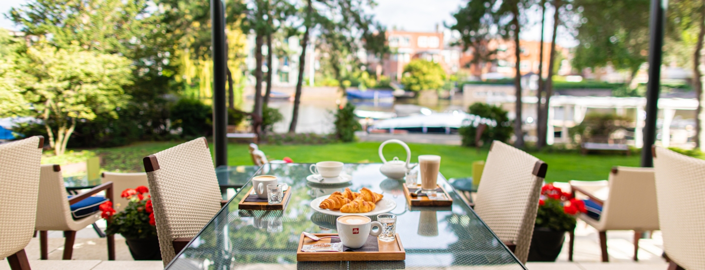 Frühstück auf einem Tisch auf einer Hotelterrasse an einem Kanal.