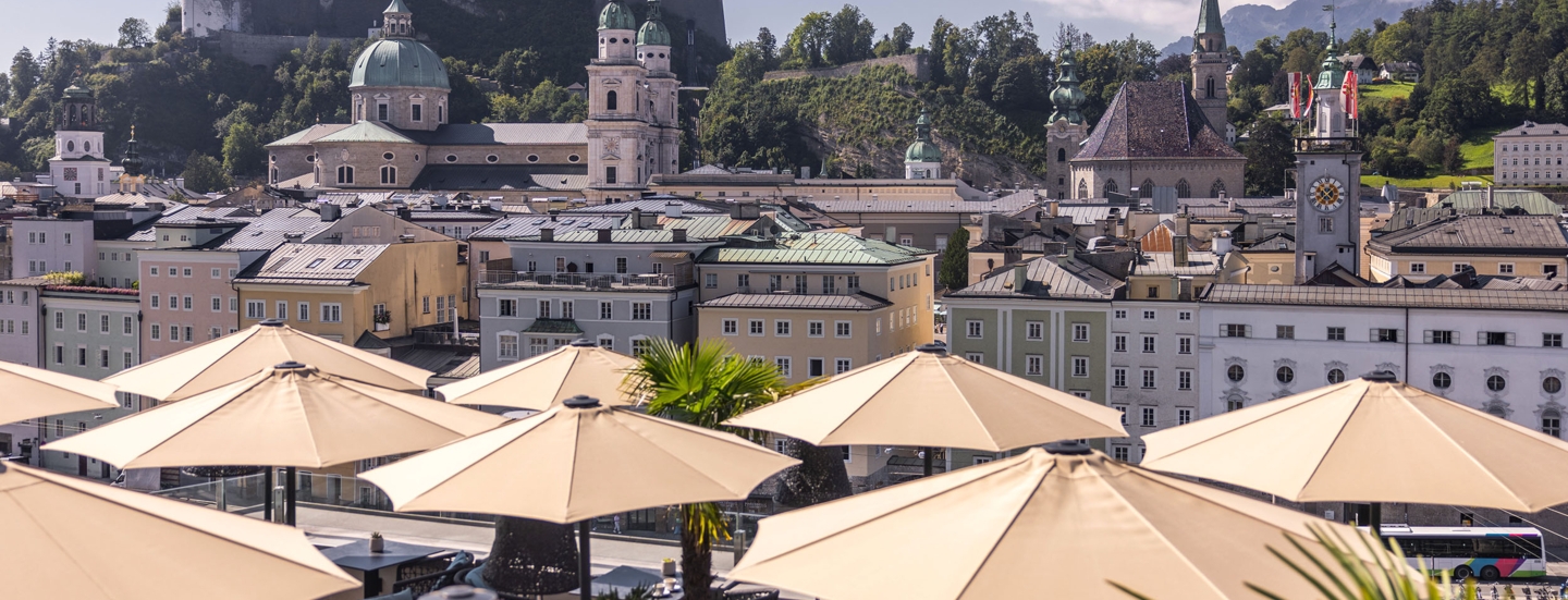 Panorama der Salzburger Altstadt mit Burg auf einem Berg am Fluss, im Hotelterrasse mit Sonnenschirmen.