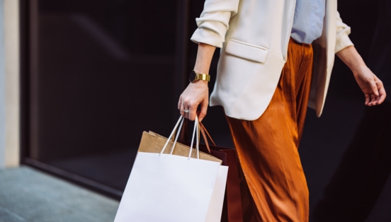 Eine angeschnittene weibliche Person in eleganter Kleidung mit Einkaufstüten in der Hand.